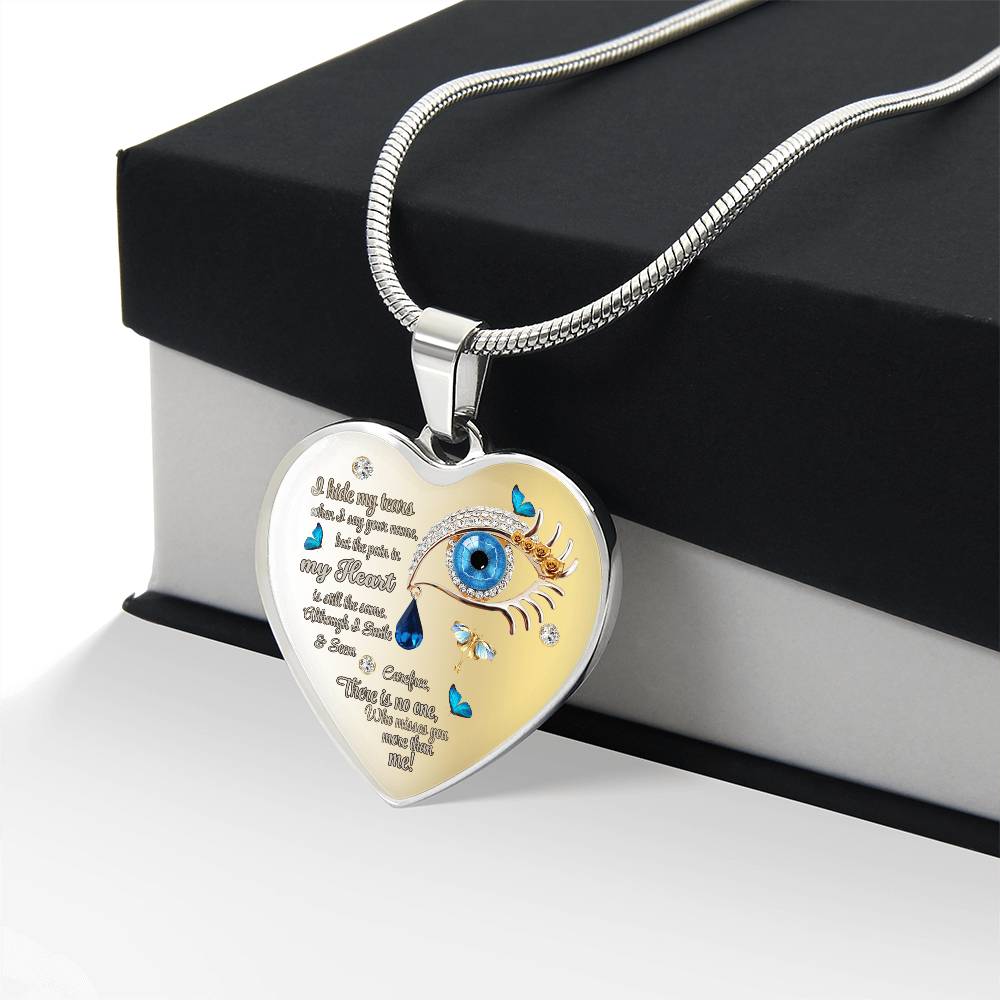 Silver heart-shaped necklace pendant engraved with a blue eye and teardrop design and poetic text on a snake chain.