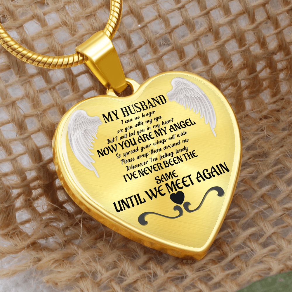 Gold heart-shaped necklace pendant engraved with angel wings and sentimental memorial text on a textured fabric background.