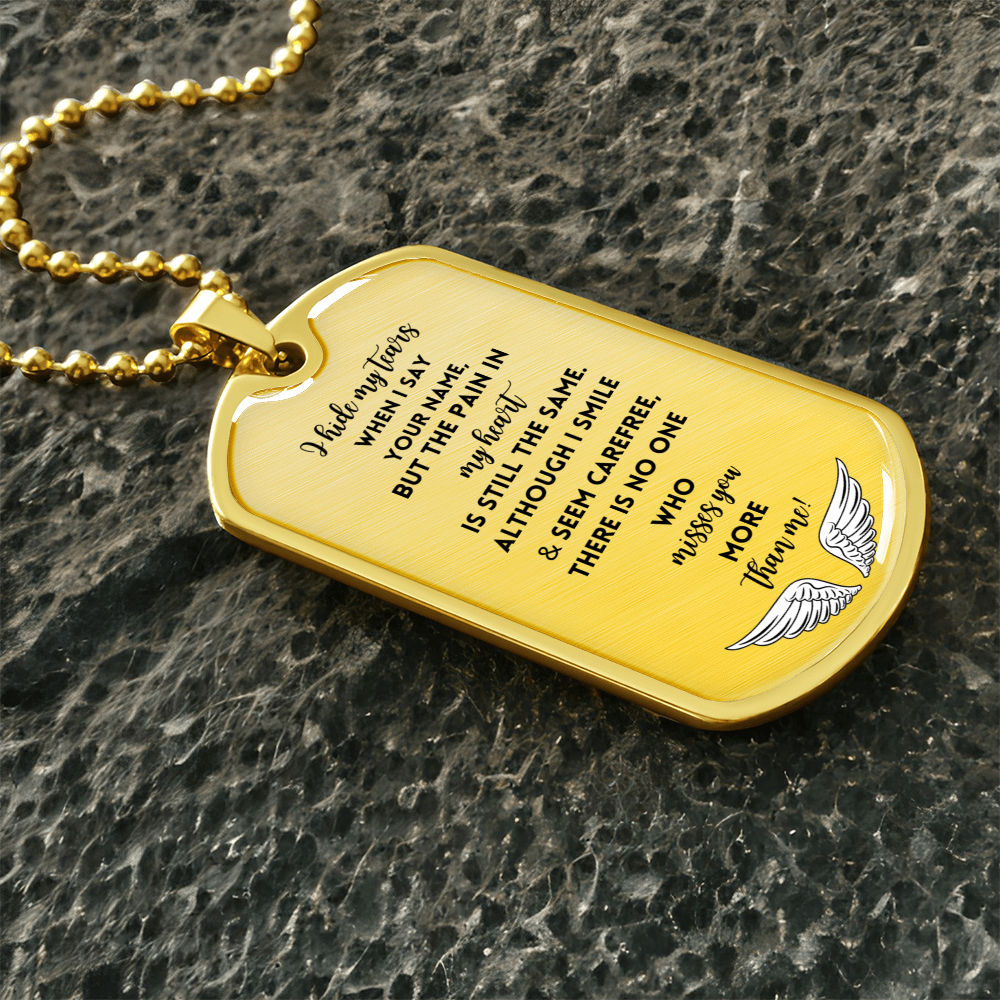 Gold-tone dog tag necklace with engraved sentimental message and angel wings design on textured dark background.