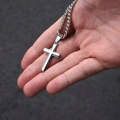 Polished stainless steel artisan cross pendant on cuban chain necklace resting in open palm, showcasing elegant design and size for husband gift