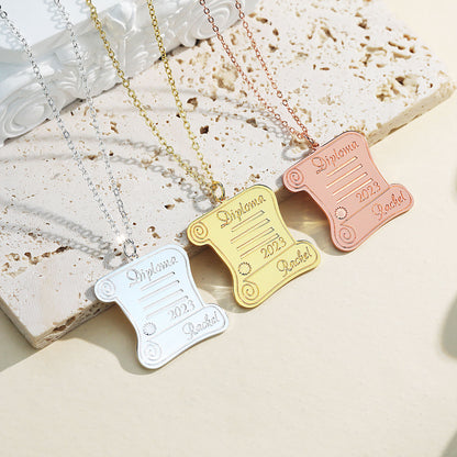 Three graduation pendant necklaces in silver, gold, and rose gold, shaped like a diploma scroll with engraved "Diploma,".