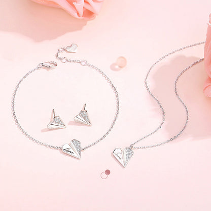 Elegant 925 Sterling Silver heart jewelry set featuring bracelet, necklace, and earrings on soft pink background with flower petals, showcasing delicate chain and sparkling gemstone accents