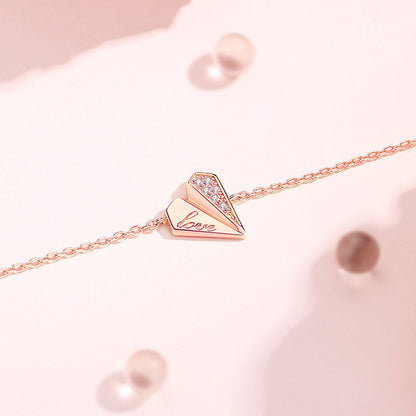 Delicate rose gold-plated sterling silver heart bracelet with 'Love' engraving and diamond accents on a fine chain, set against a soft pink background with pearl-like elements