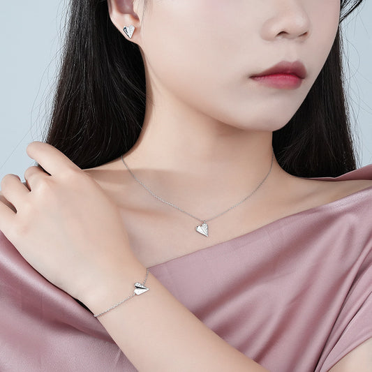 Elegant 925 Sterling Silver Heart Jewelry Set: delicate necklace and bracelet with heart-shaped pendants, paired with matching heart stud earrings. Showcased on model wearing soft pink satin top, highlighting the versatile and feminine design.