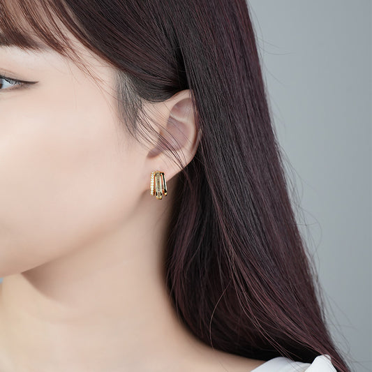 Elegant gold-plated 925 sterling silver earrings worn by a woman with dark hair, showcasing their fashionable design and small size. The earrings feature a unique curved shape, adding a touch of sophistication to the wearer's appearance.