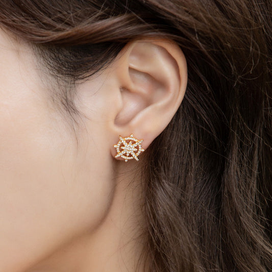 Gold-plated sterling silver ship's wheel earring worn on ear, showcasing intricate nautical design with spokes and center detail, against dark hair background