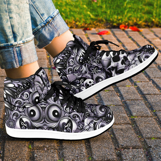 High-top sneakers with black and white skull and eye design worn on a paved surface.